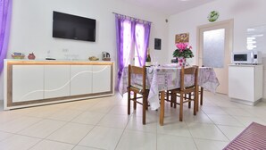 A modern kitchen with a built-in microwave, a dining table with chairs, and a TV mounted on the wall. - IzzHome Regina Margherita (Pula)