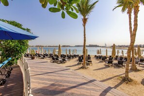 Area relax in spiaggia con lettini, palme e ombrelloni.