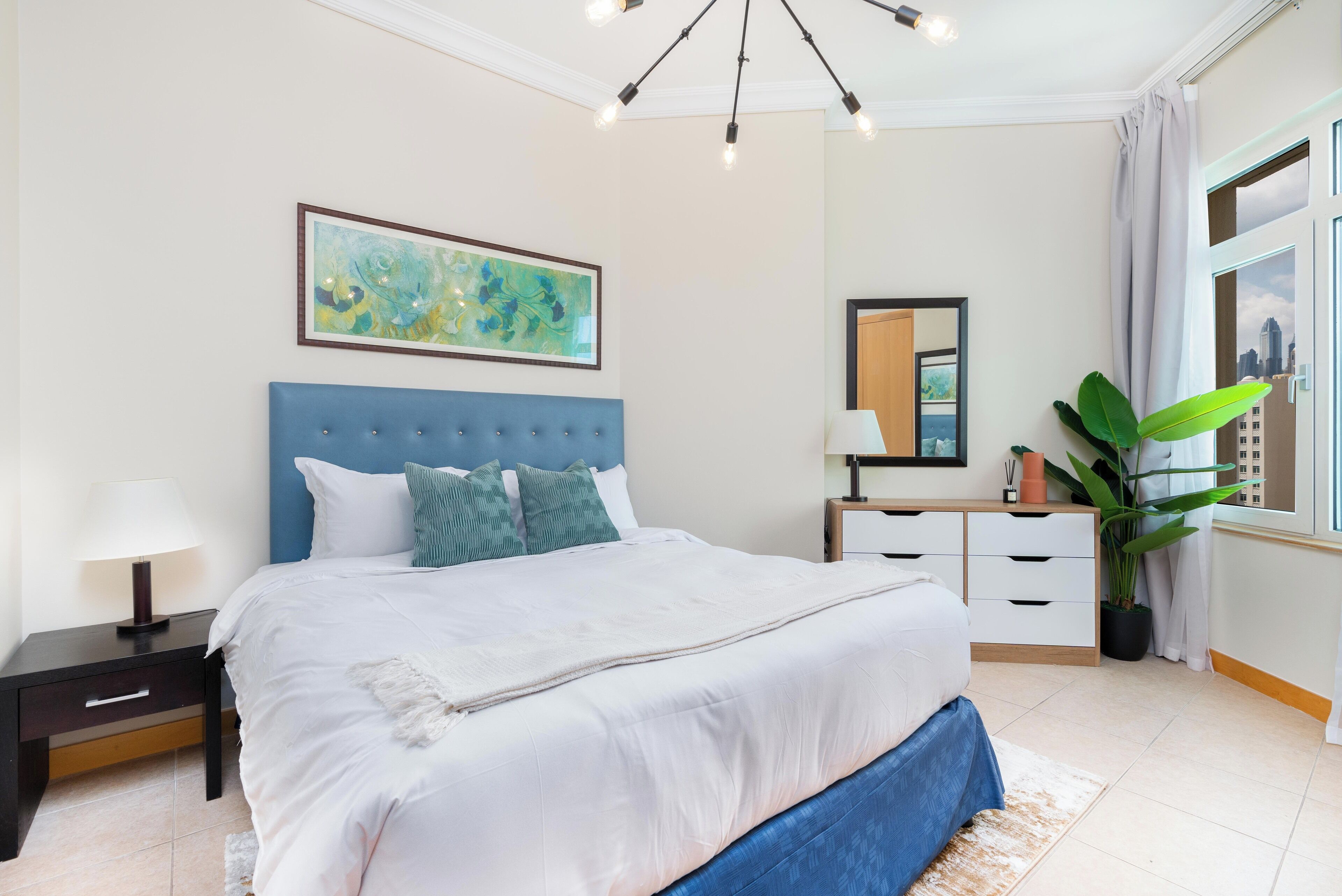 Een slaapkamer met een groot bed, een nachtkastje, een kaptafel, een spiegel en een raam met uitzicht over de stad.