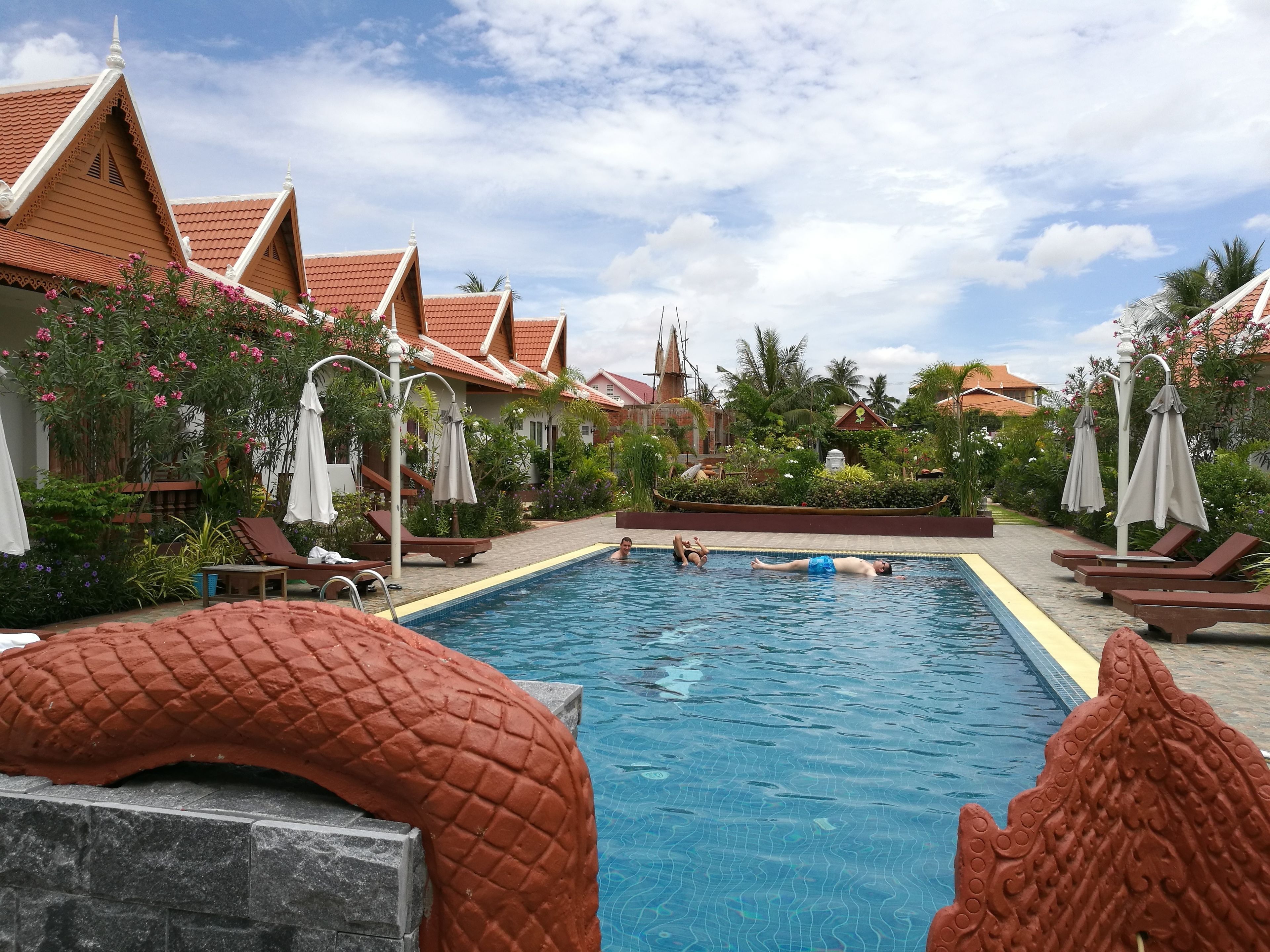 Una piscina con techos de azulejos, sillas de descanso y sombrillas.