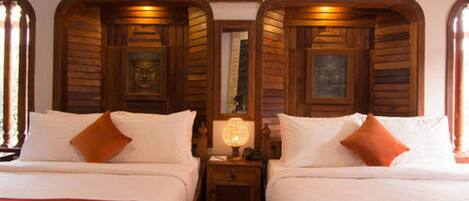 A hotel room with two beds, wooden headboards, a nightstand with a lamp, and a framed picture on the wall.