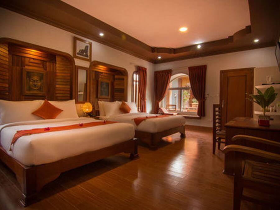 A hotel room with two beds, wooden headboards, a desk, and a chair.