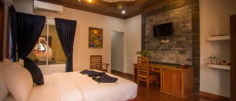 A hotel room with a large bed, wooden furniture, a stone wall, and a flat-screen TV.