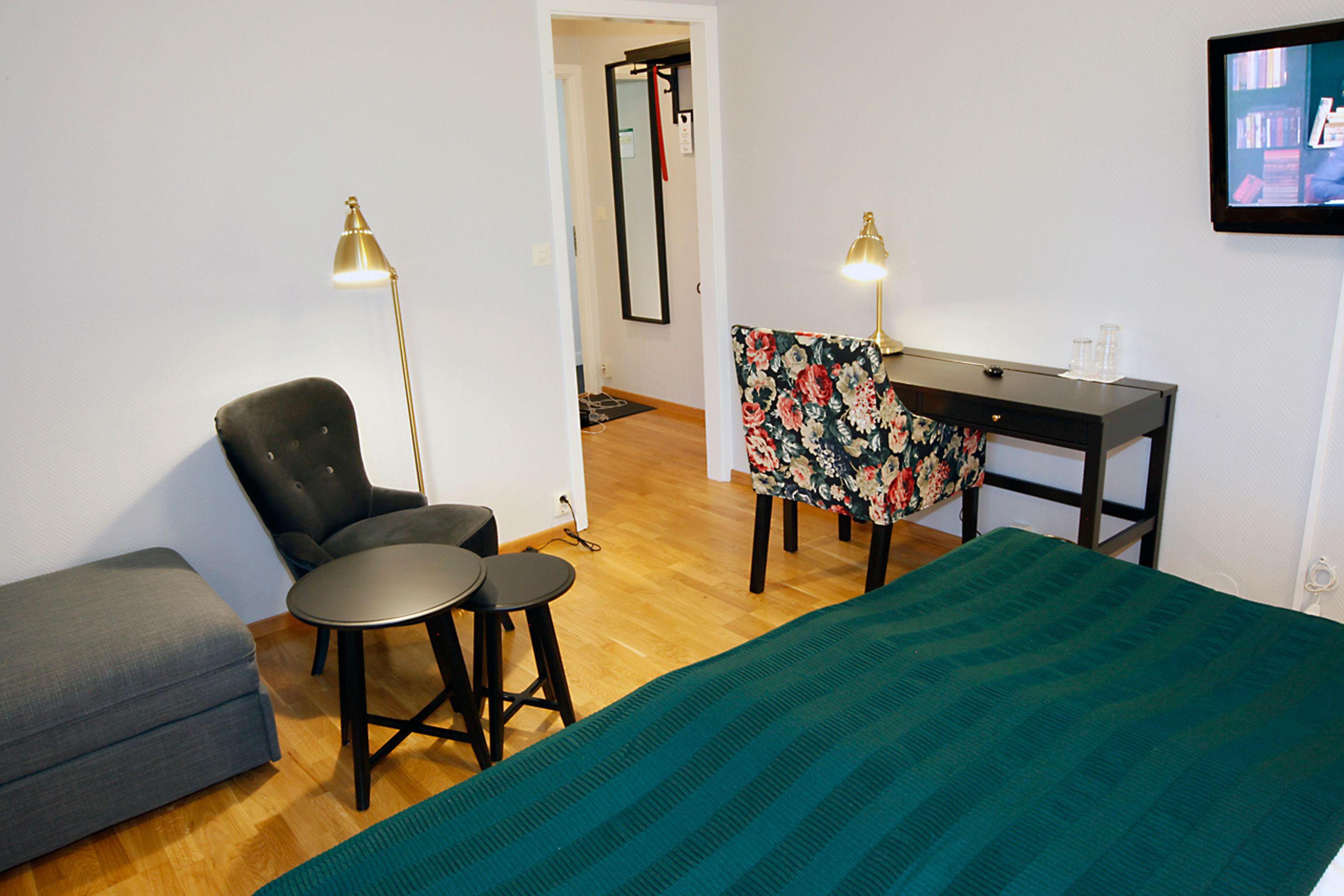 Ein Zimmer mit einem Bett, einem Schreibtisch, zwei Sesseln, einem Sofa und zwei Stehlampen.