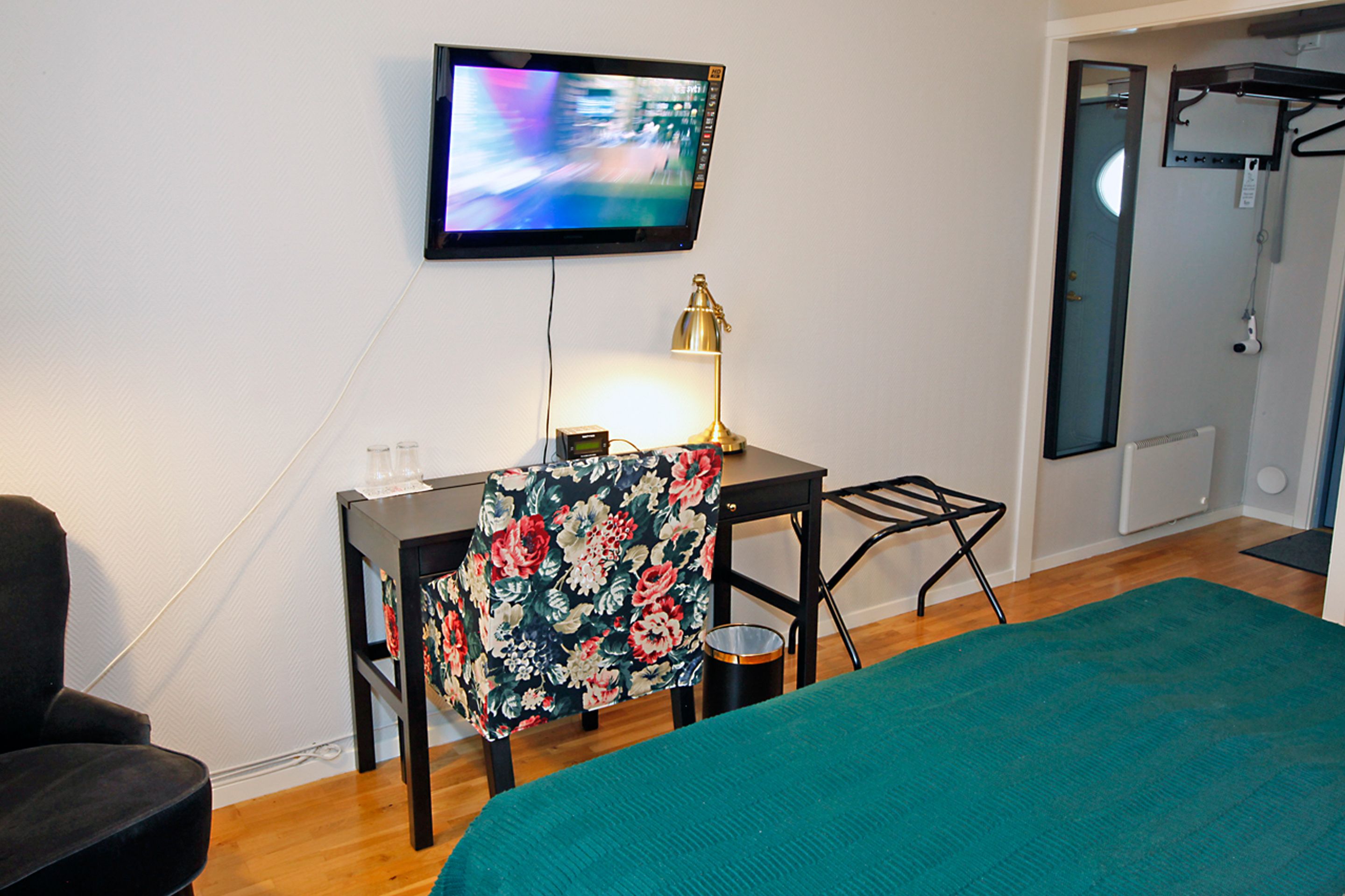 A hotel room with a bed, a desk with a chair, a television mounted on the wall, and a bathroom door.