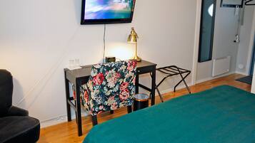 A hotel room with a bed, a desk with a chair, a television mounted on the wall, and a bathroom door.