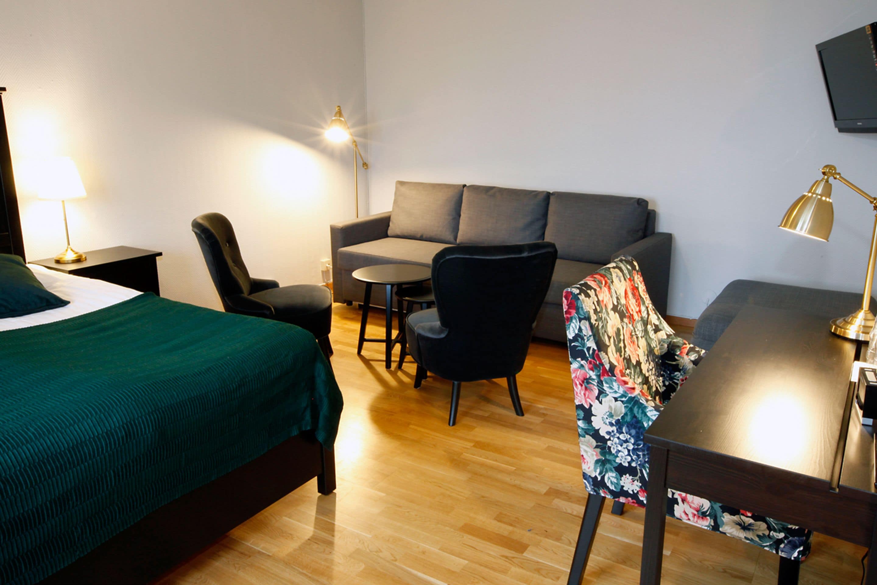 A hotel room with a bed, a sofa, a desk, a chair, and a TV mounted on the wall.