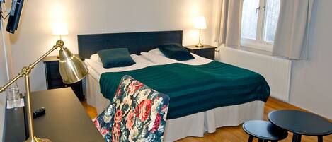 A hotel room with a bed, two bedside lamps, a desk with a lamp, a chair, and a small table.