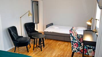 A compact room with a bed, two chairs, a small table, and a desk.