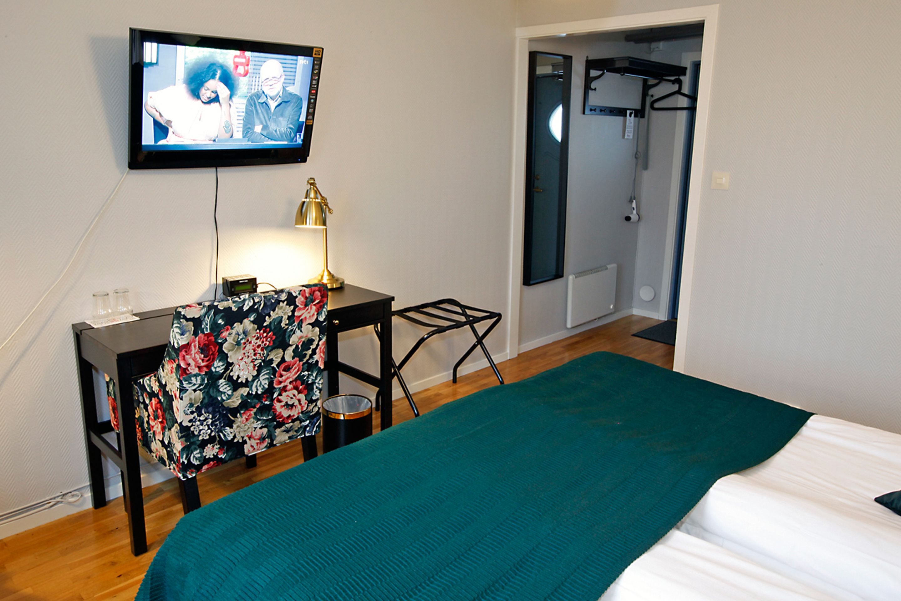 Une chambre d’hôtel avec un lit, un bureau doté d’une lampe, une télévision et une salle de bain visible à travers une porte ouverte.