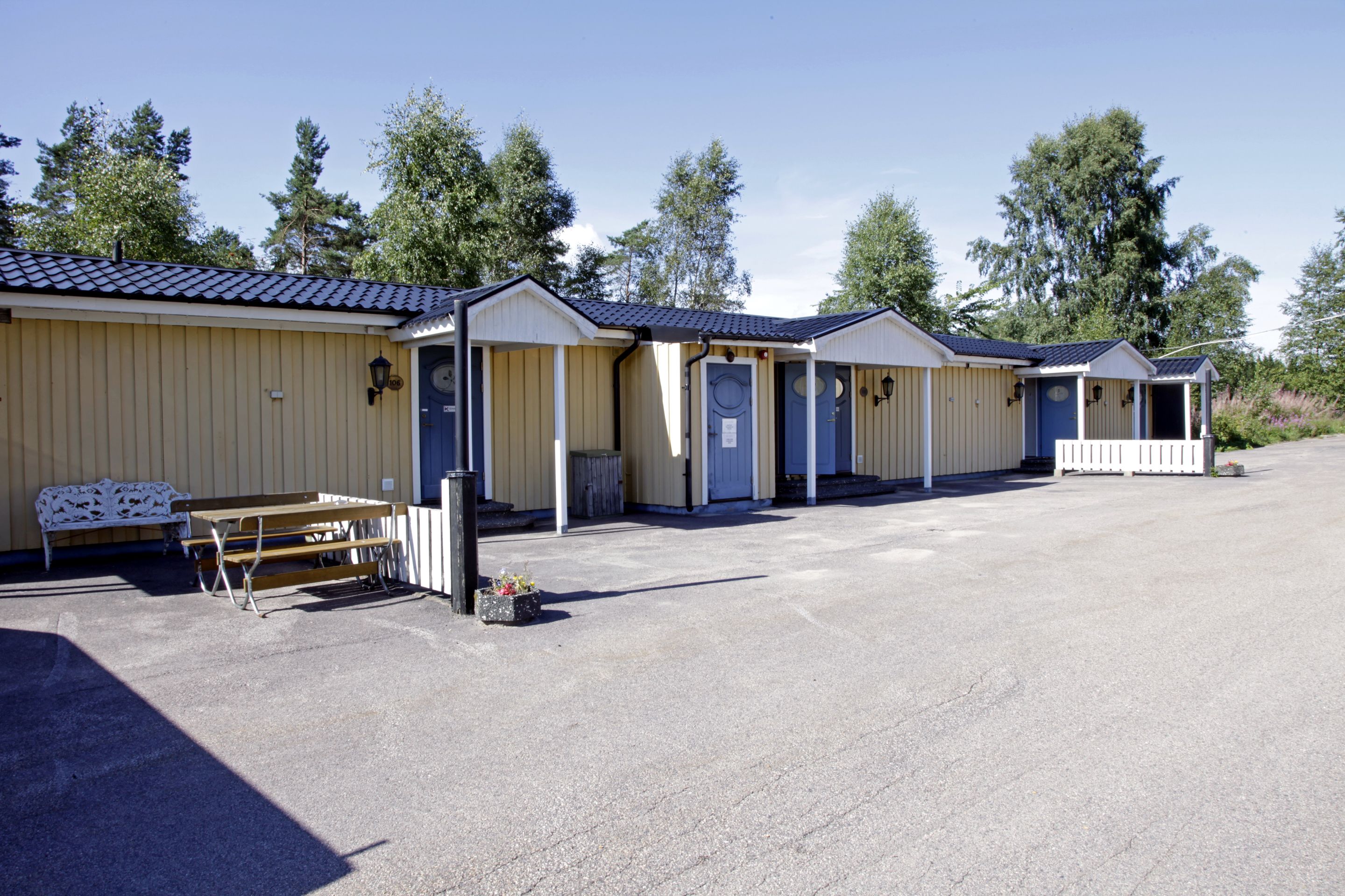 A row of single-story cabins with a covered outdoor area, a bench, and a table.