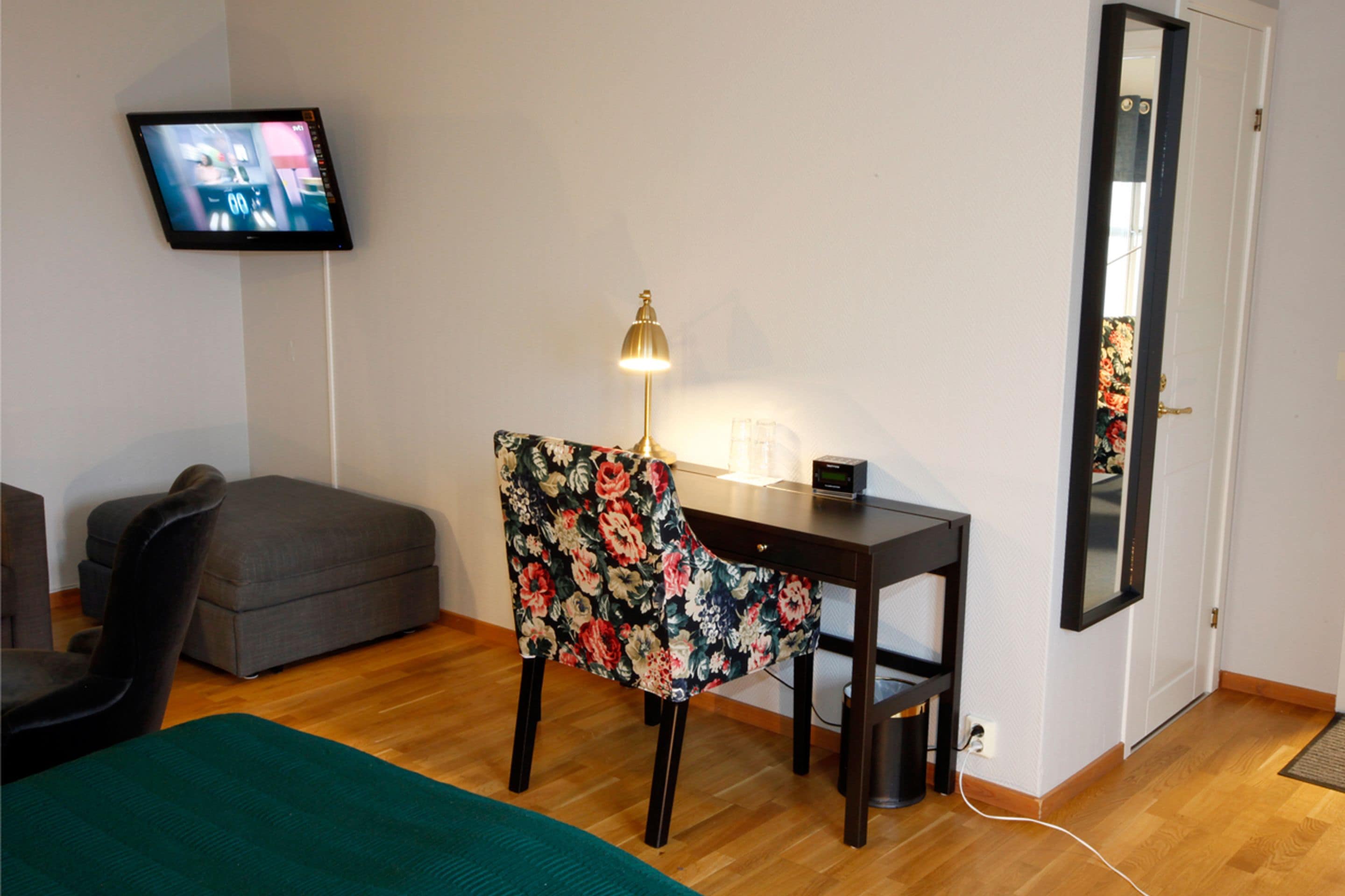 Une chambre comprenant un lit, un bureau avec une chaise, un téléviseur fixé au mur et un miroir sur la porte.