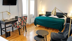 A hotel room with a bed, two bedside lamps, a desk with a chair, a TV, and a small table. - Rasta Hallandsåsen (Ostra Karup)