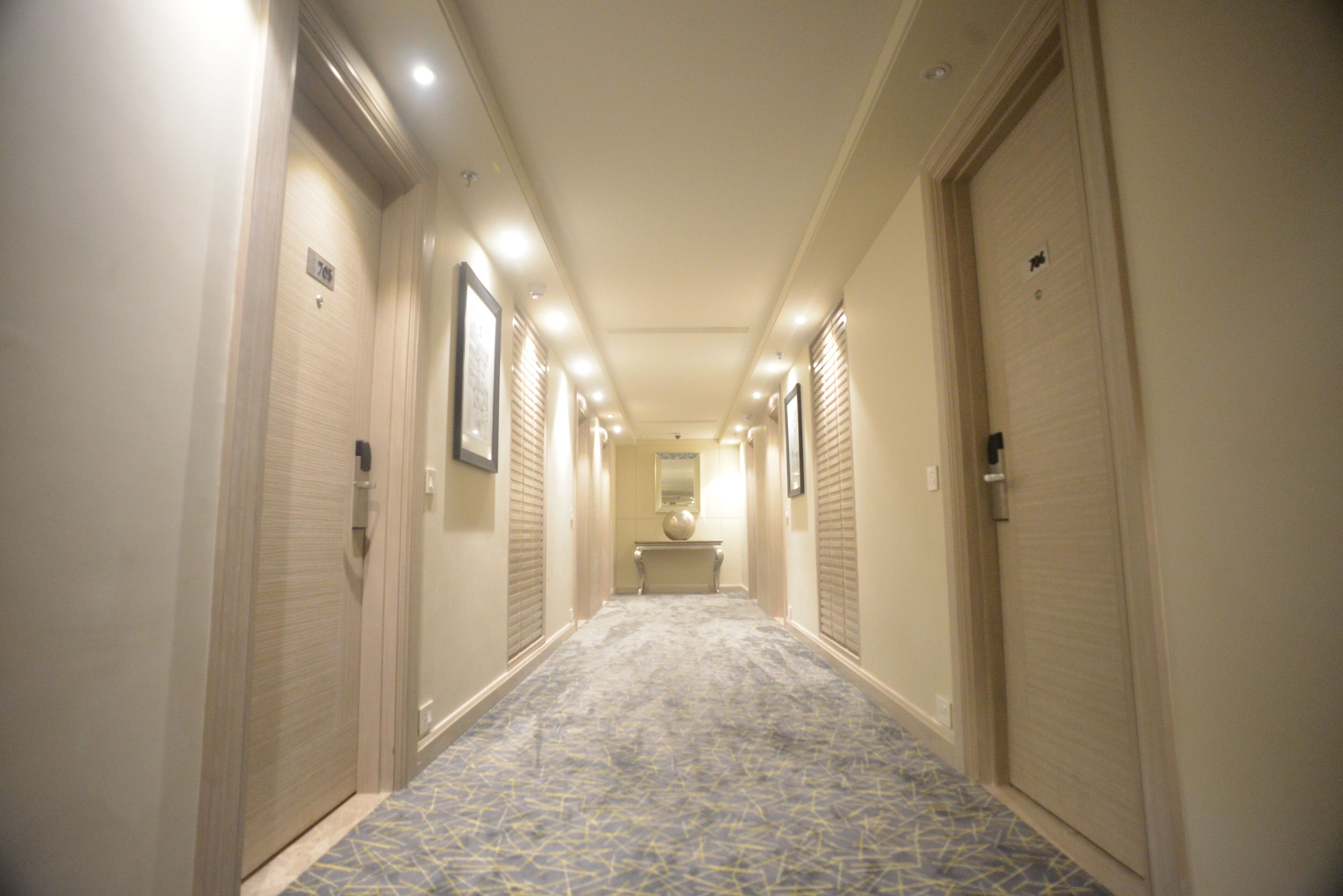 A hotel hallway with a patterned carpet, closed doors, and a central light fixture.