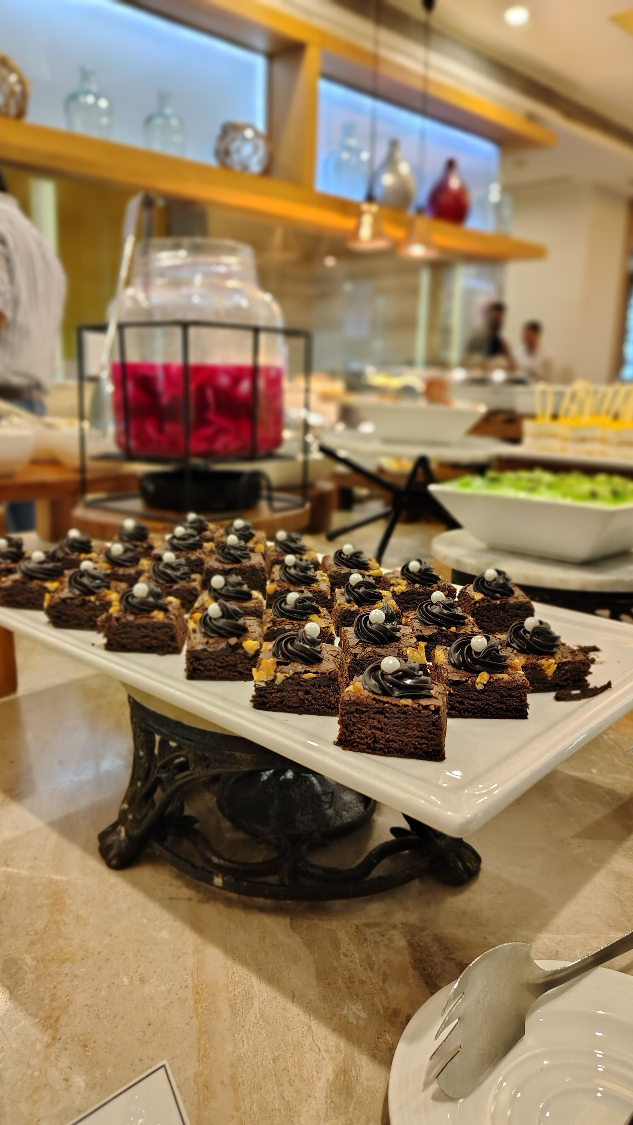 A buffet table with various desserts, including brownies and a large jar of pink liquid.