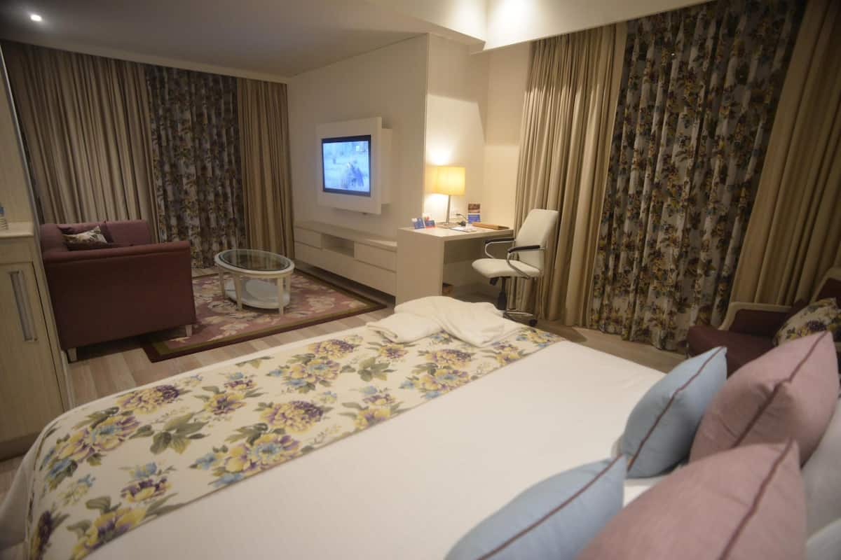 Hotellihuone, jossa on sänky, työpöytä, tuoli, televisio ja verhot.