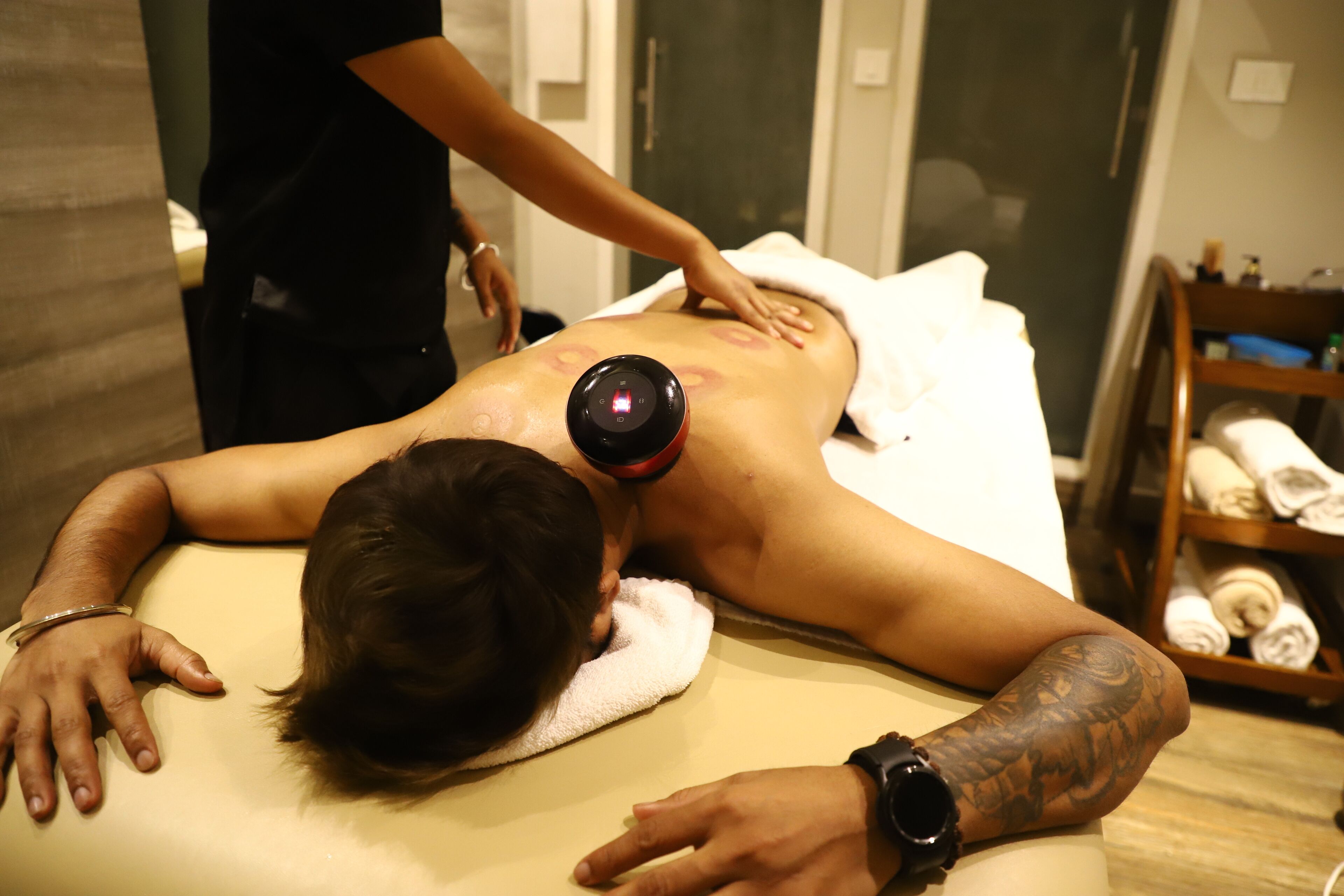 A massage therapy session in a room with a wooden floor, a shelf with towels, and a door in the background.