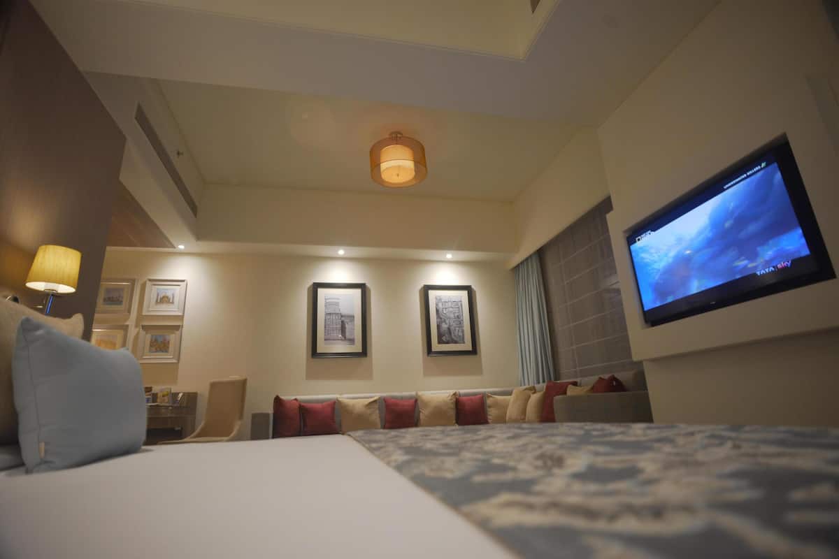 Hotellihuone, jossa on sänky, televisio, seinällä taulut ja kattovalaisin.