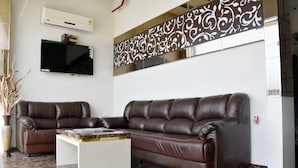 Una sala de estar moderna con dos sofás de cuero marrón, un televisor de pantalla plana, un panel decorativo y piso de mármol.