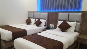 Habitación de hotel con dos camas, cada una con cabecero de madera y ropa de cama blanca. Hay una mesita de noche con un teléfono y una botella de agua.