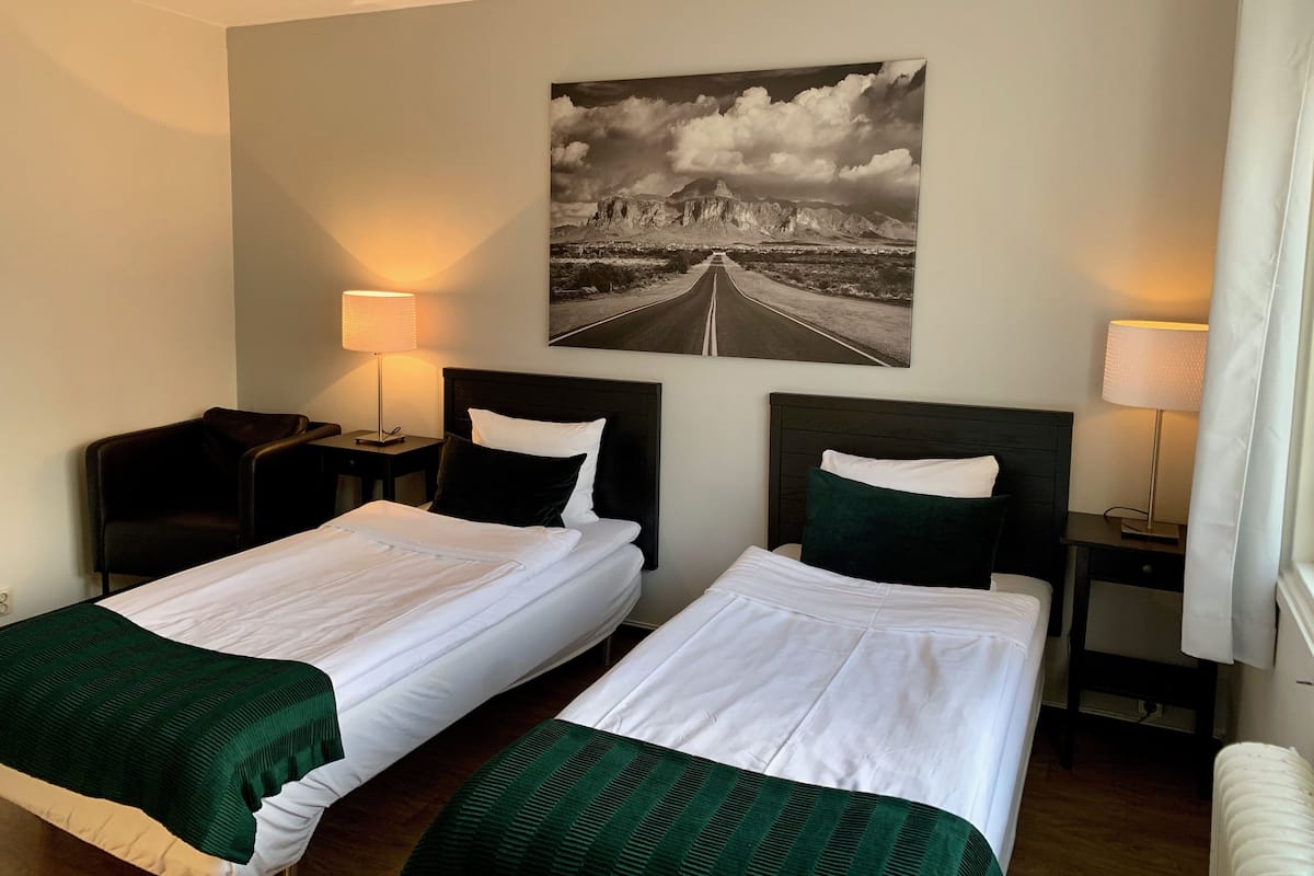 Habitación de hotel con dos camas individuales, un cuadro grande en la pared que muestra una carretera, y dos mesitas de noche con lámparas.