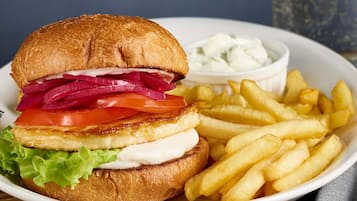 A burger with lettuce, tomato, red onion, and cheese, served with French fries and a side of sauce.