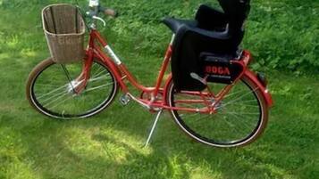 A red bicycle with a basket and a black seat bag parked on grass.