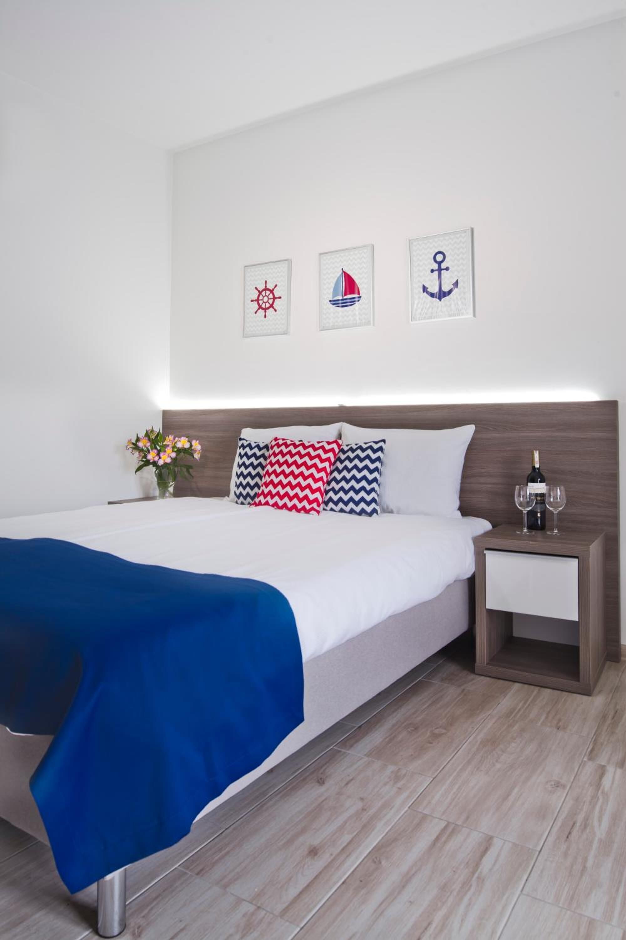 A neatly made bed with a blue blanket, a bedside table with a bottle and glasses, and three wall-mounted nautical-themed pictures.