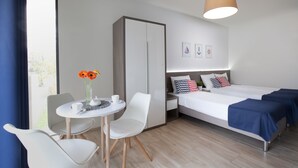 Ein modernes Hotelzimmer mit Bett, zwei Nachttischen, einem Sessel, einem kleinen Tisch mit Blumenvase und einem Fenster mit Vorhängen.