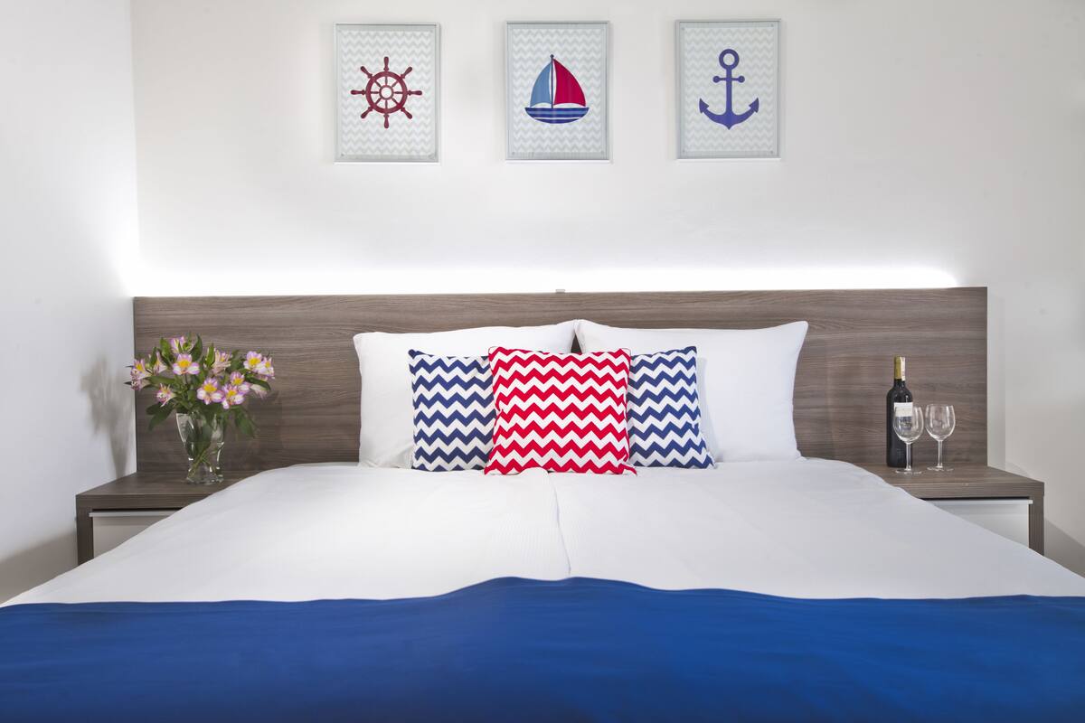 A neatly made bed with a blue and white bedspread, a wooden headboard, and decorative pillows. There is a vase with flowers on the nightstand beside the bed.