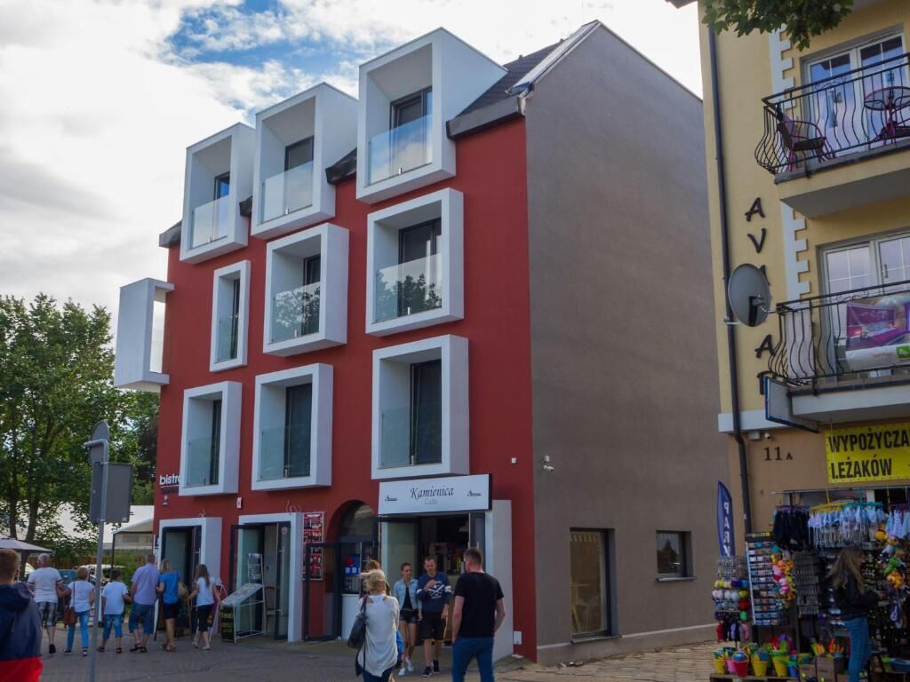 Ein modernes Gebäude mit zahlreichen Fenstern und Balkonen, einem sichtbaren Schaufenster und einer Straße mit Fußgängern.