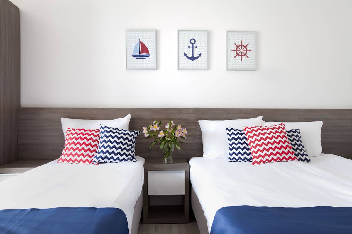 A hotel room with two beds, each with white bedding and navy blue bedspreads. There are three framed nautical-themed pictures on the wall.