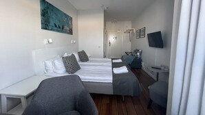 A hotel room with two beds, a desk, a chair, a TV, and a painting on the wall.