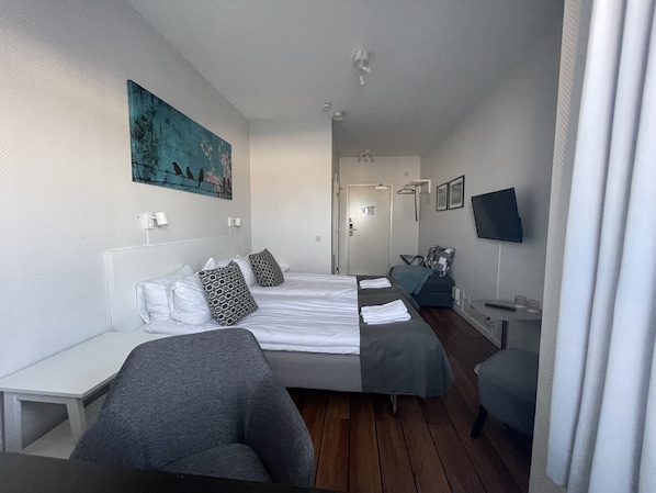 A hotel room with two beds, a desk, a chair, a TV, and a painting on the wall.