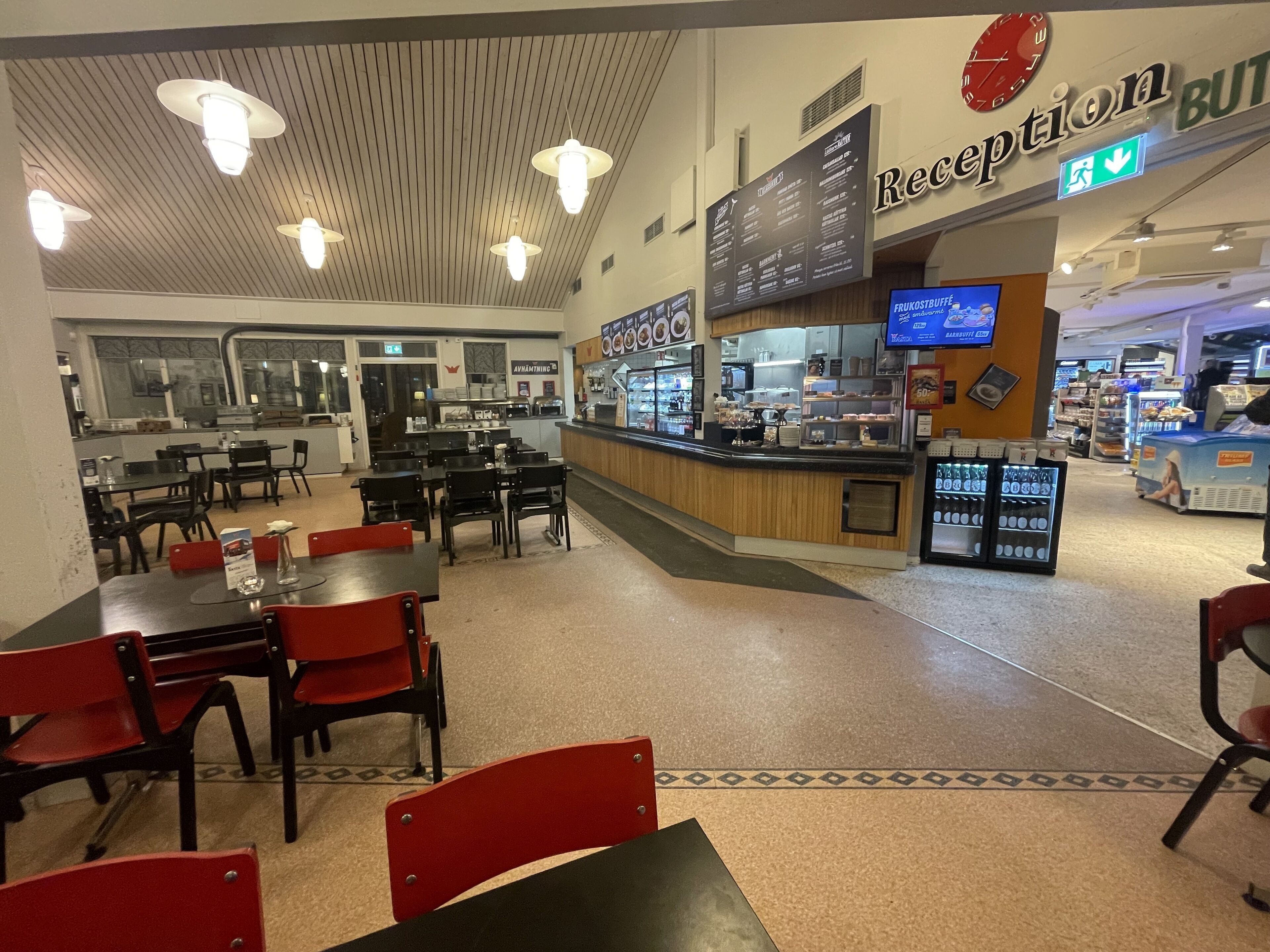 En cafeteria med bord och stolar, en reception och en disk med en meny.