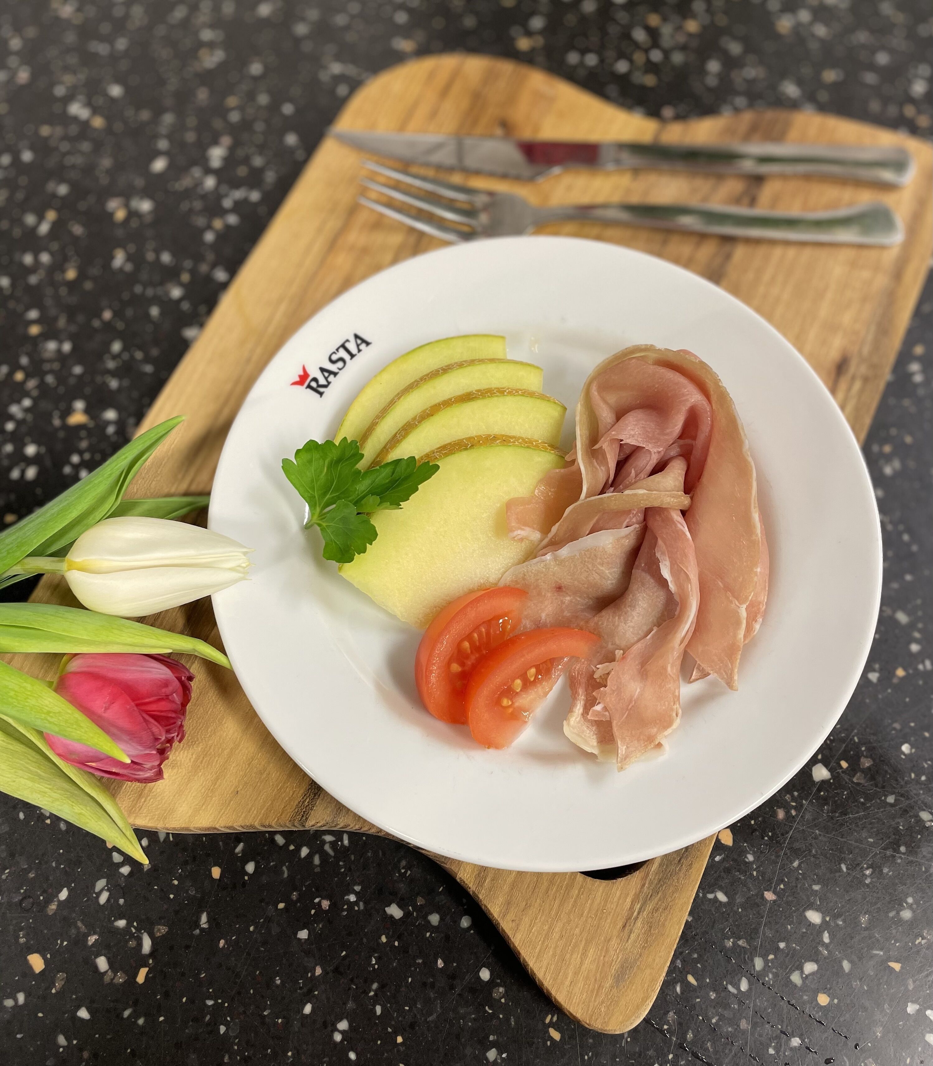 Un plato con rodajas de manzana, jamón y tomates sobre una tabla de madera.