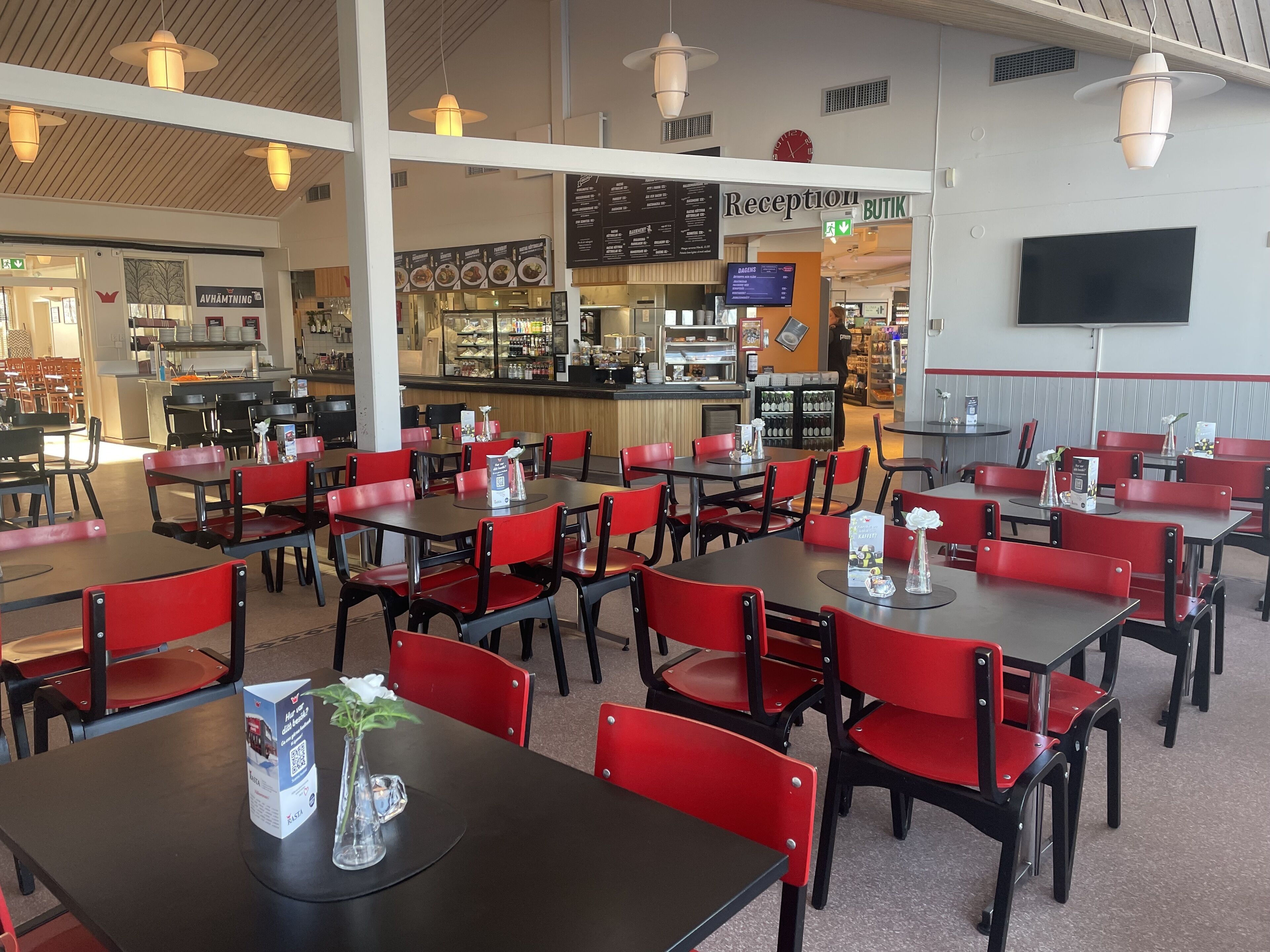 Un restaurante con sillas rojas y mesas negras, una zona de recepción y un tablero de menú.