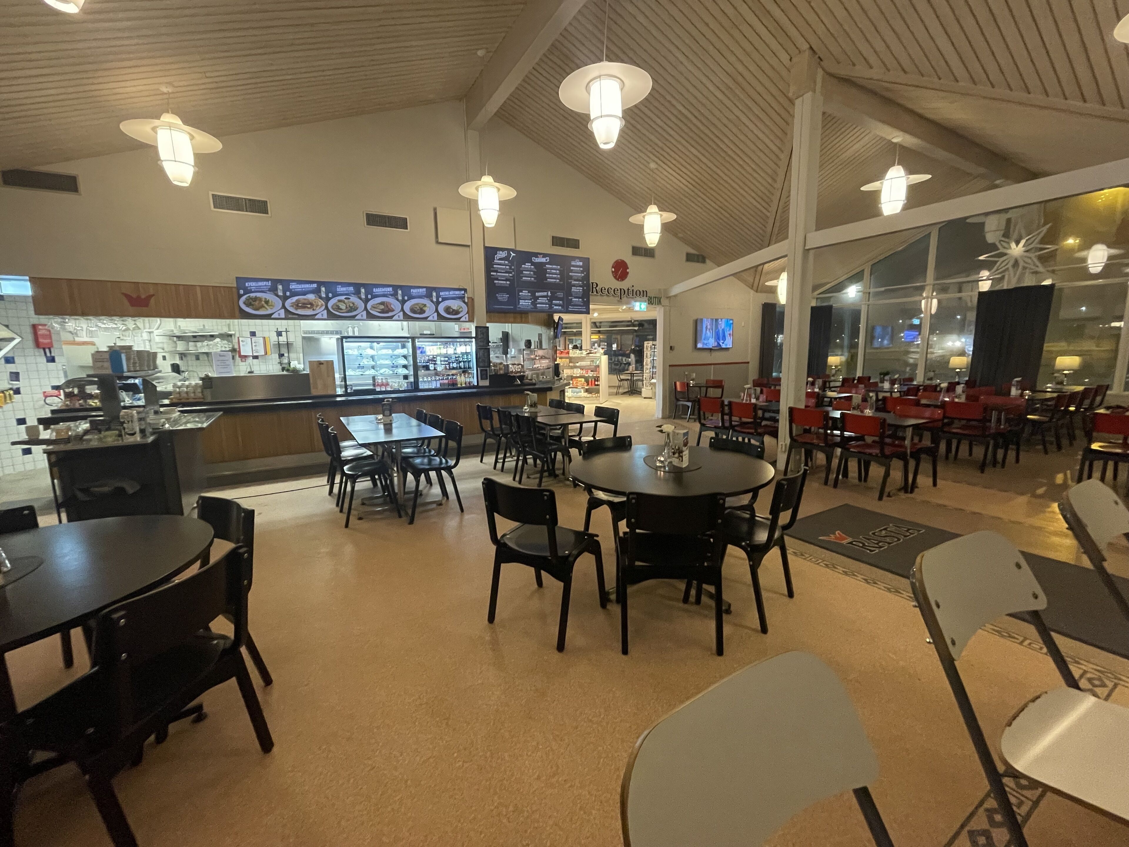 Un restaurant doté d’un bar, de tables et de chaises. On peut voir des panneaux affichant le menu au-dessus du bar et un comptoir d’accueil à l’arrière-plan.