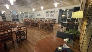 A restaurant with wooden flooring, multiple tables and chairs, and hanging pendant lights.