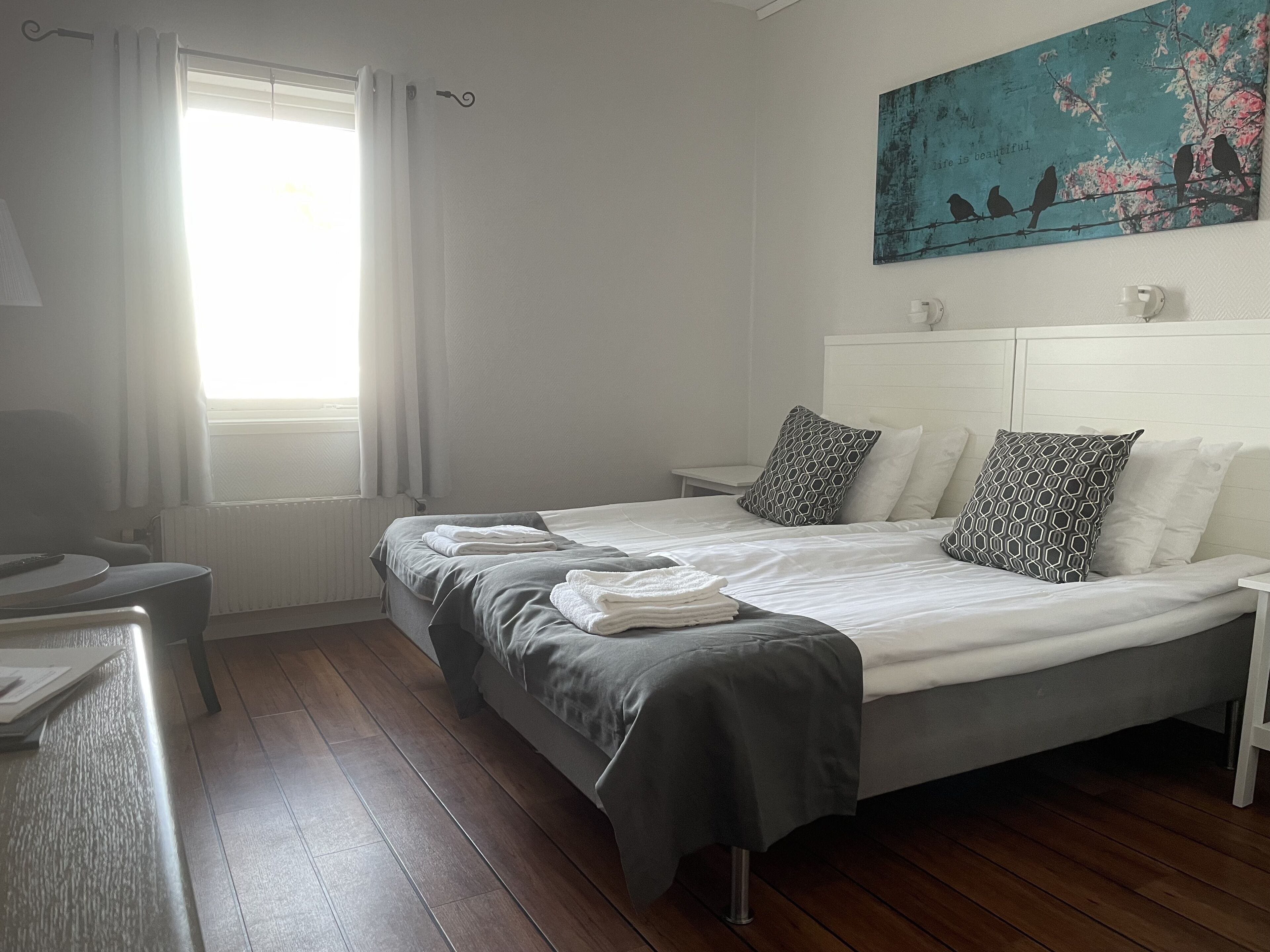 A neatly arranged bedroom with a bed, bedside tables, and a painting on the wall.