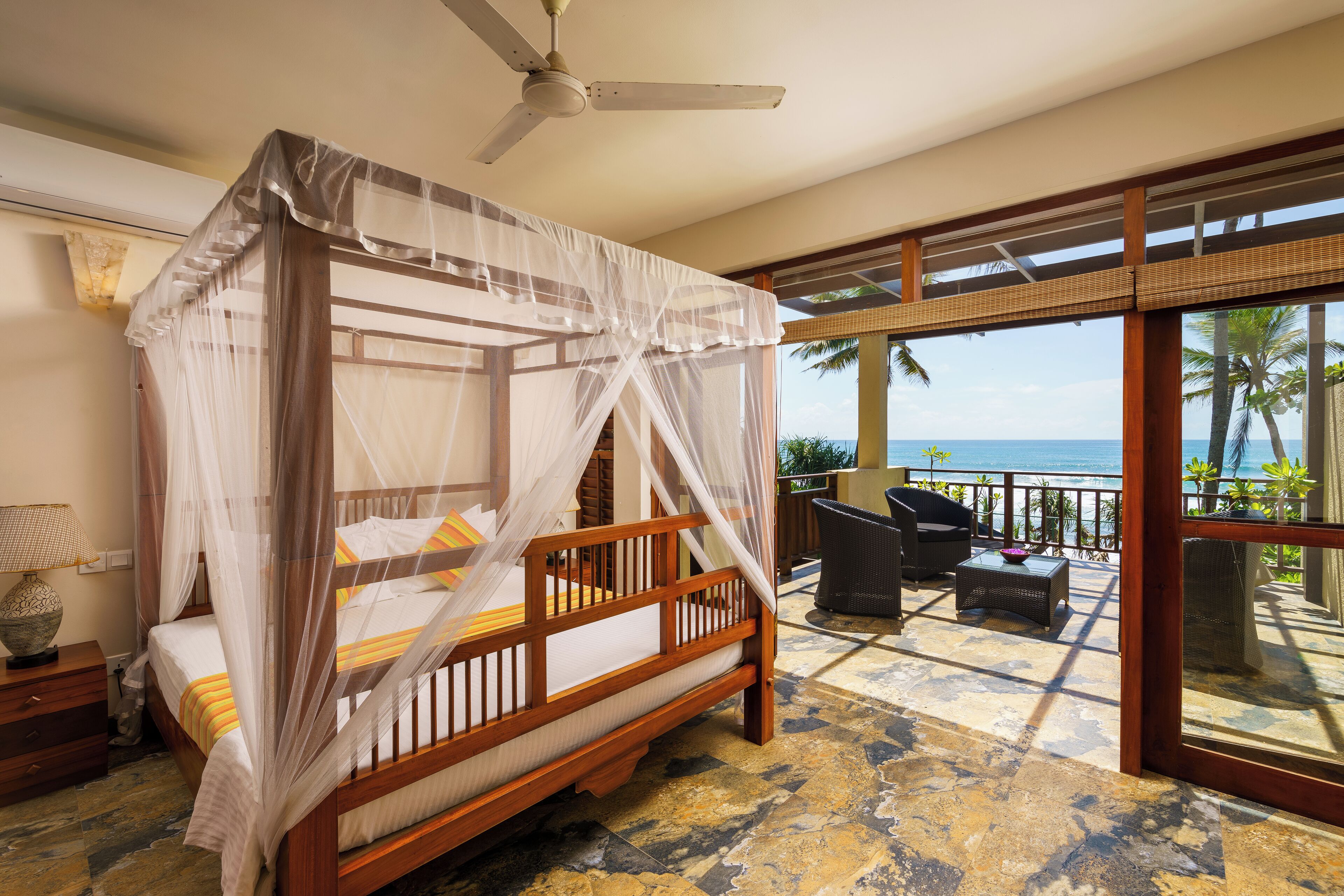 A four-poster bed with a canopy, a ceiling fan, and a view of the ocean.