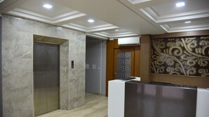 A modern elevator with a metallic finish, a reception desk with a decorative panel, and a ceiling with recessed lighting.