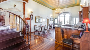 A spacious living area with a wooden staircase, a dining table with chairs, a kitchen area with a sink and countertop, and a chandelier.