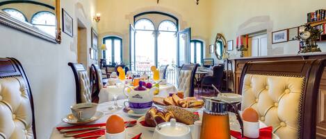 A breakfast setting with a table set for two, featuring eggs, bread, and beverages.