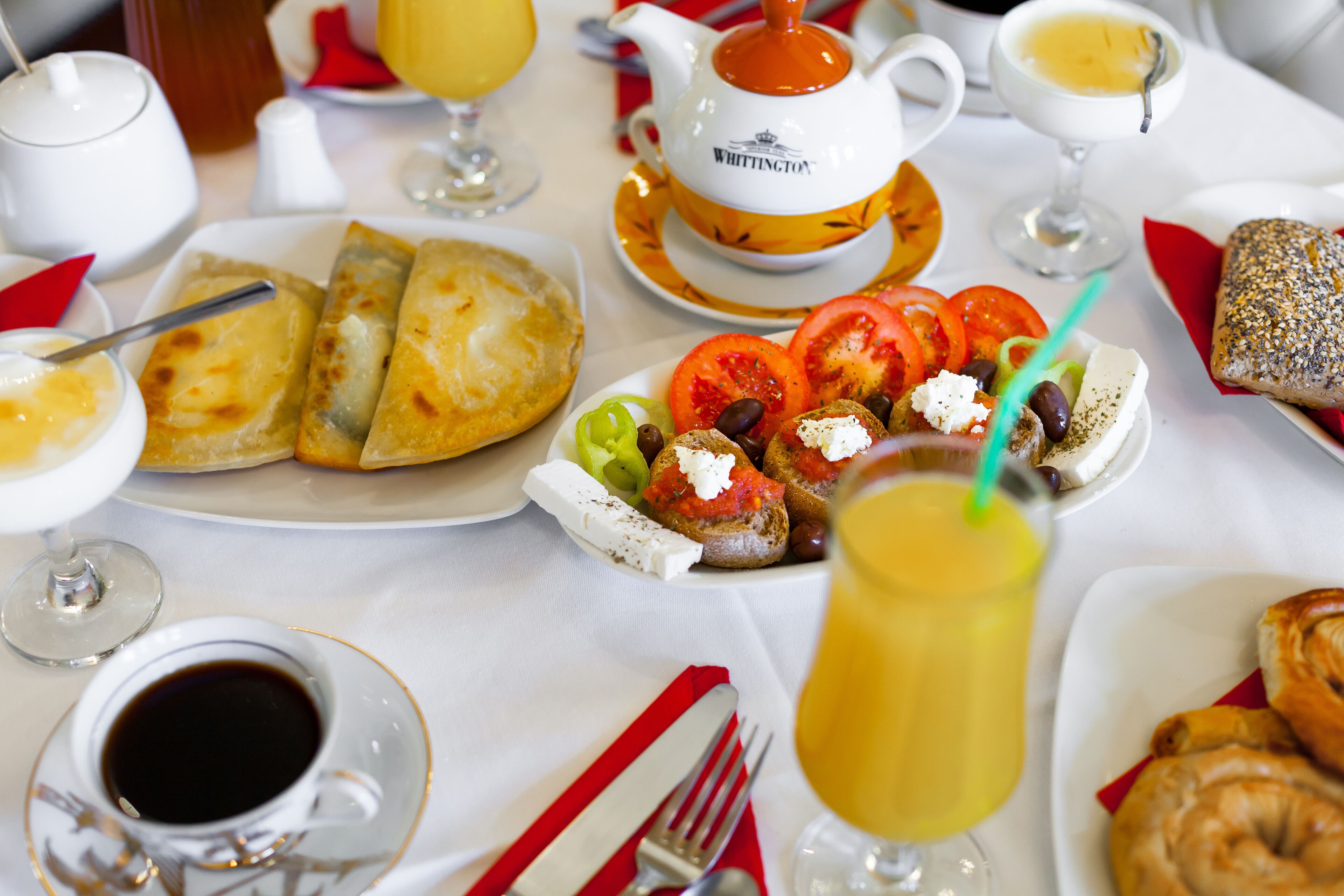 Un desayuno con diversos platos, como cruasanes, tomates, aceitunas y queso, además de tazas de café y té.