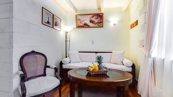 Een woonkamer met een bank, een stoel, een ronde salontafel met fruit en ingelijste foto's aan de muur.