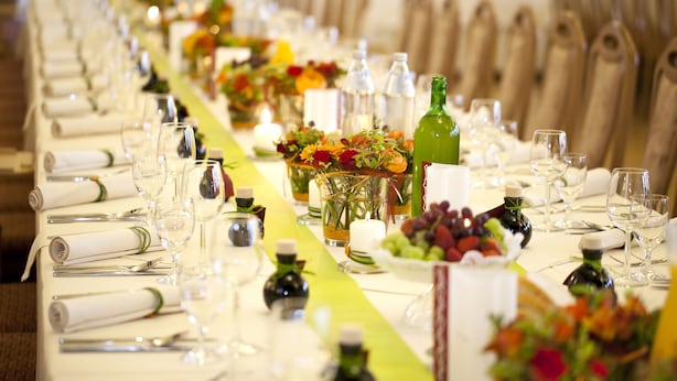 Una larga mesa de comedor adornada con copas, servilletas dobladas y centros de mesa con flores.