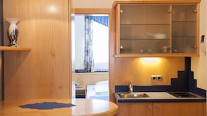 Una cocina de hotel compacta con armarios de madera, un lavamanos y un pequeño comedor.