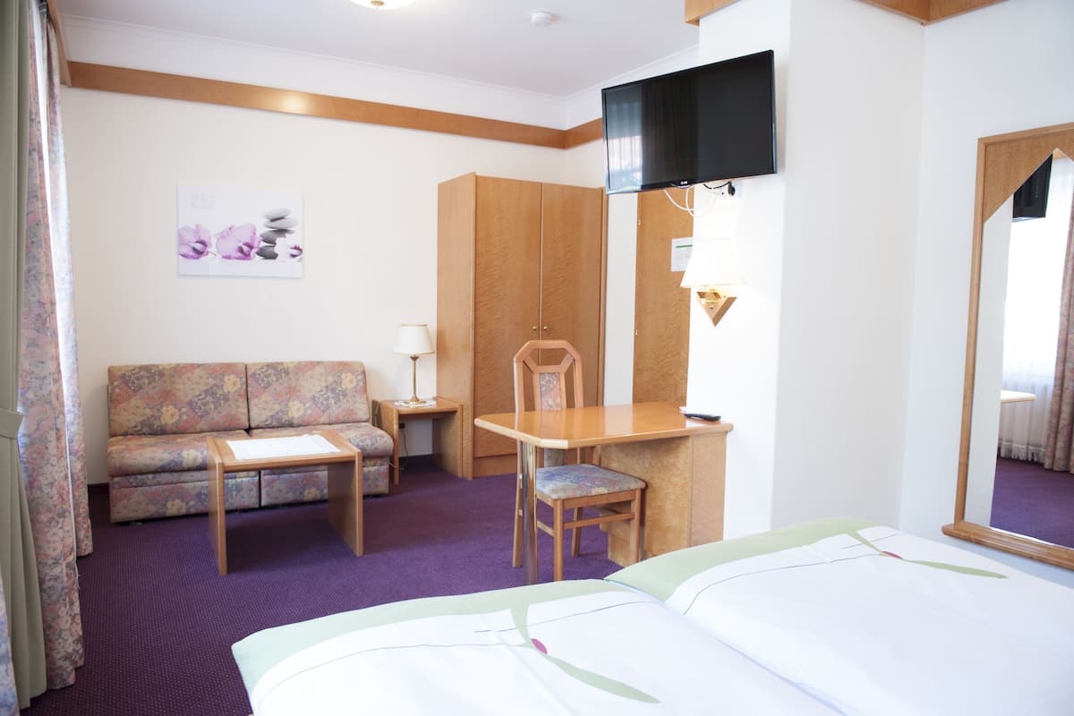 Una habitación de hotel con cama, escritorio, silla, sofá y televisión.