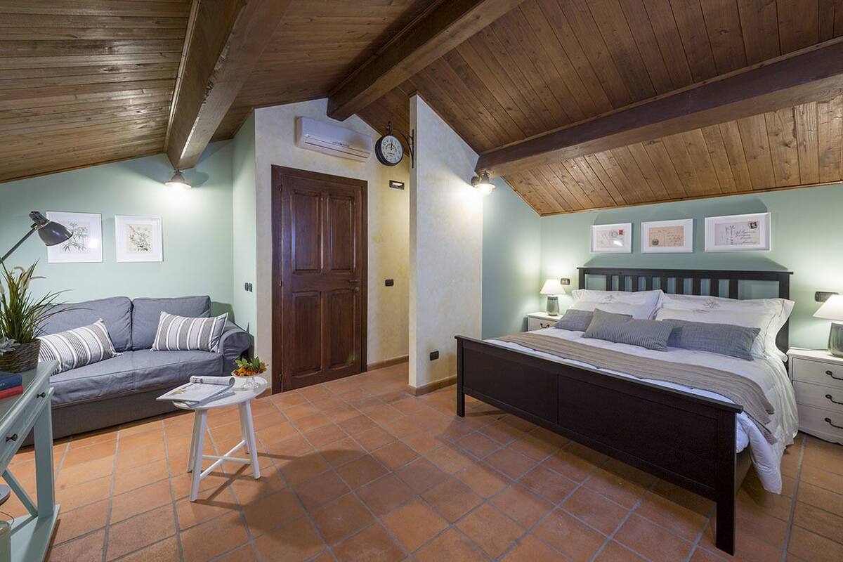A bedroom with a bed, a sofa, a small table, and a nightstand.